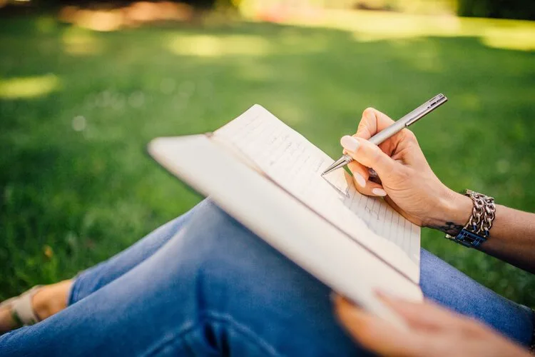 Person journaling in a notebook while sitting on the grass