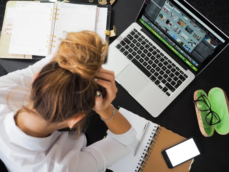 Stressed woman holding her head over a laptop and planner, seen from above