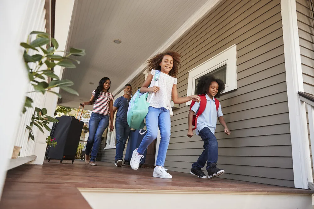 Family with suitcases and backpacks heading out the front door for vacation