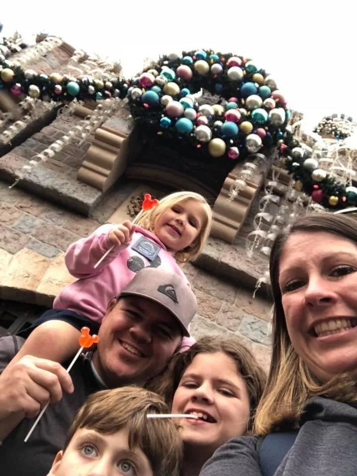 Family selfie beneath holiday ornament garland on a PGAV team member's theme park trip