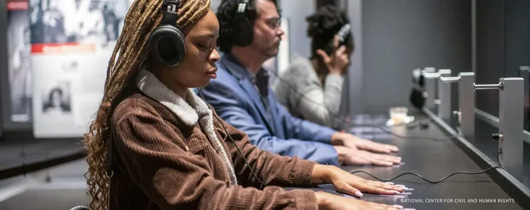 Visitors wearing headphones seated at the Lunch Counter Sit-In simulation