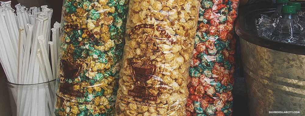 Bags of kettle corn and flavored popcorn beside straws and a drink tub at Silver Dollar City