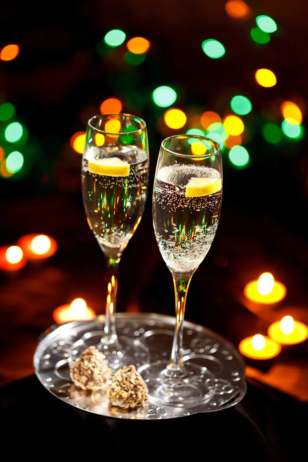 Two glasses of champagne and chocolates on a silver tray with candles and festive lights
