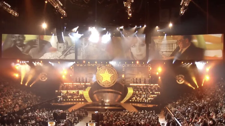 Arena stage show with a large star set piece, bright lights and a full audience