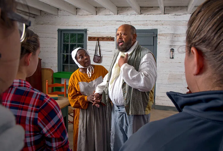 Costumed interpreters portraying 19th-century characters speaking with visitors inside a cabin at Conner Prairie
