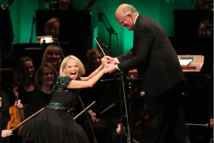 Kristin Chenoweth performing joyfully with an orchestra and its conductor on stage