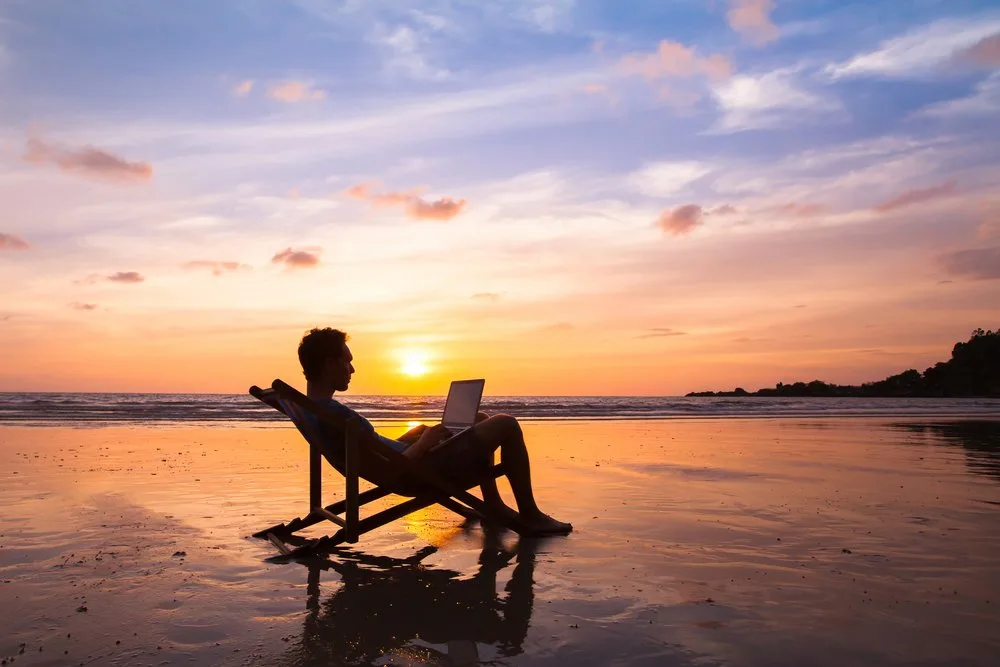 Silhouette of a man working on a laptop in a beach chair at sunset