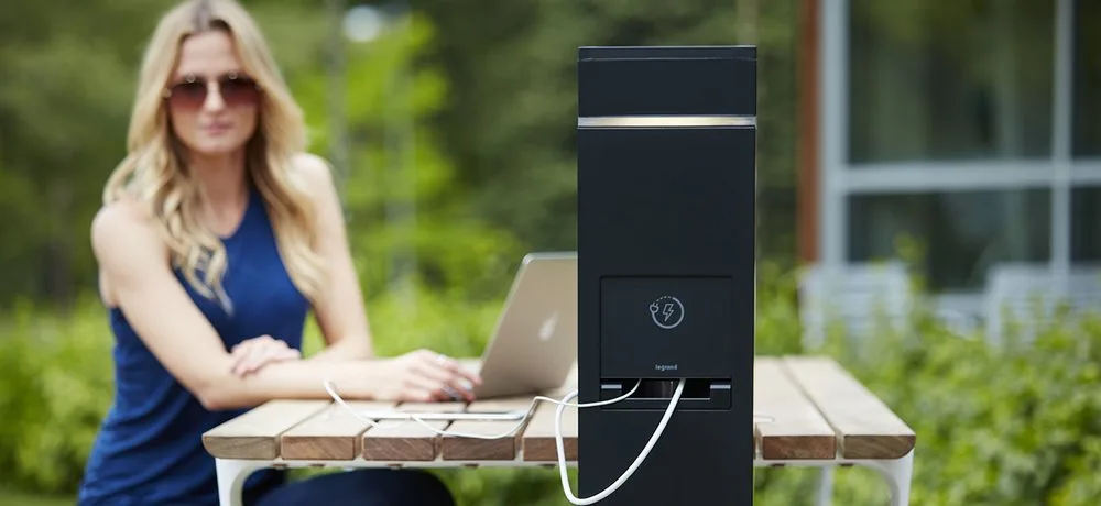 Woman working on a laptop at an outdoor table with a built-in charging post