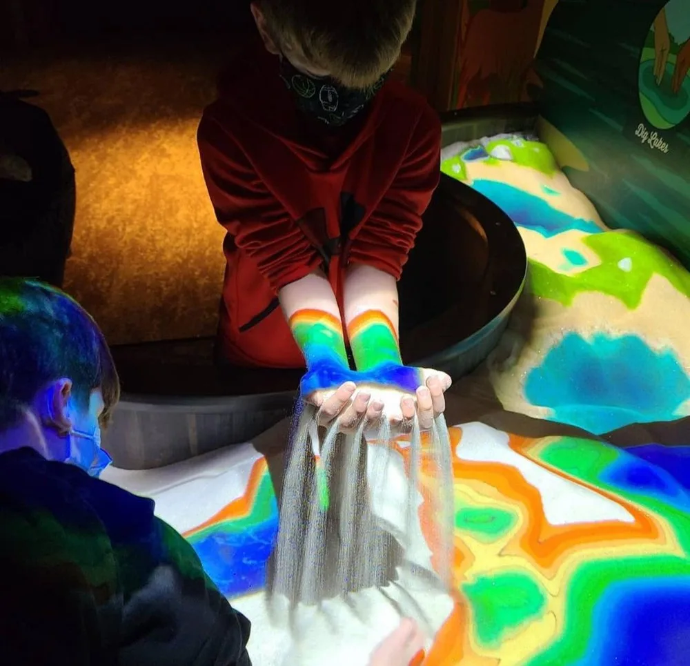 Child letting sand run through their hands over a colorful projected-topography sandbox