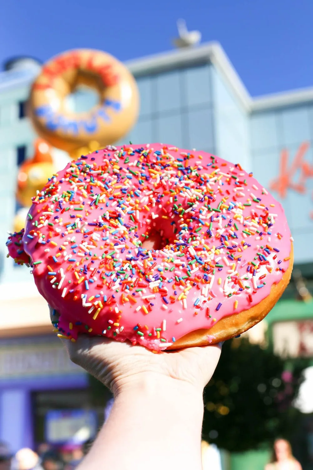 Hand holding a giant pink sprinkled Lard Lad donut at Universal Studios Hollywood