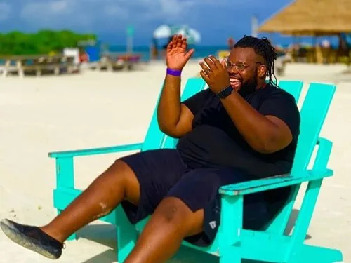 Laughing traveler relaxing in a turquoise Adirondack chair on a sunny beach