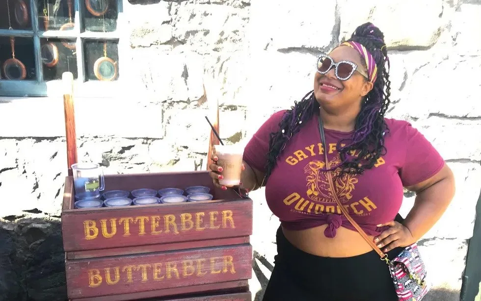Smiling theme park visitor in a Gryffindor Quidditch shirt holding a drink beside a Butterbeer cart