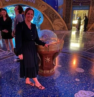 Woman standing beside an ornate globe pedestal on a starry, polished floor in a themed attraction