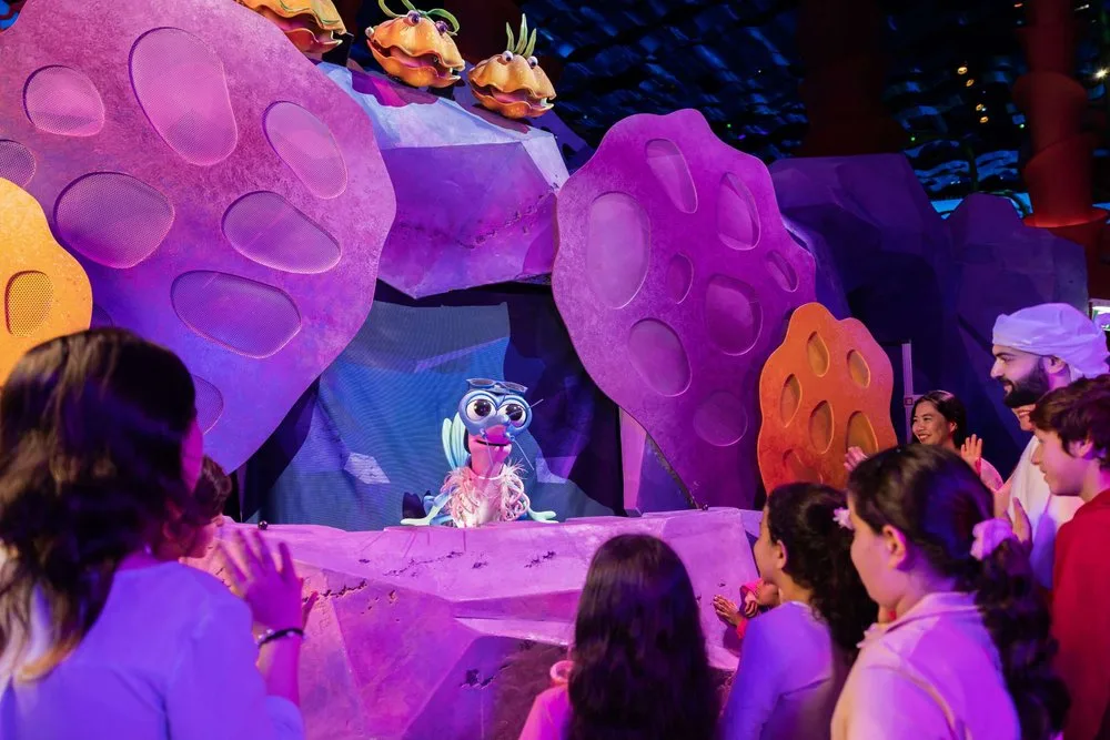 Children watching an animated krill character show in a colorful coral-themed theater at SeaWorld Abu Dhabi