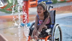 Laughing girl in a wheelchair playing in the fountains of a splash pad