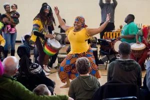 Dancer in African print clothing performing with drummers for a seated audience