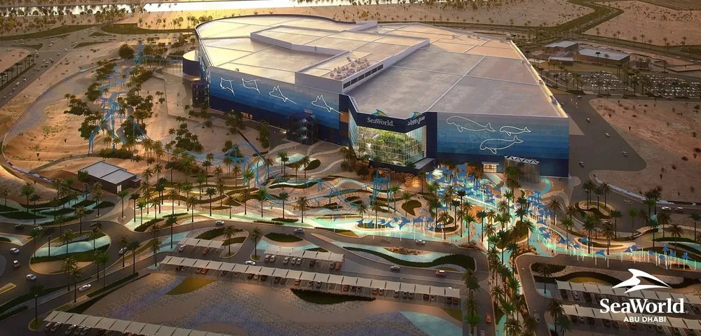 SeaWorld Abu Dhabi aerial rendering showing the main building, palm-lined plaza and parking at sunset