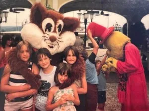 Children hugging costumed characters in a vintage family photo at a theme park