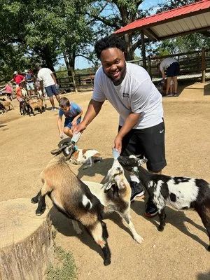 Man feeding a group of goats at a petting zoo