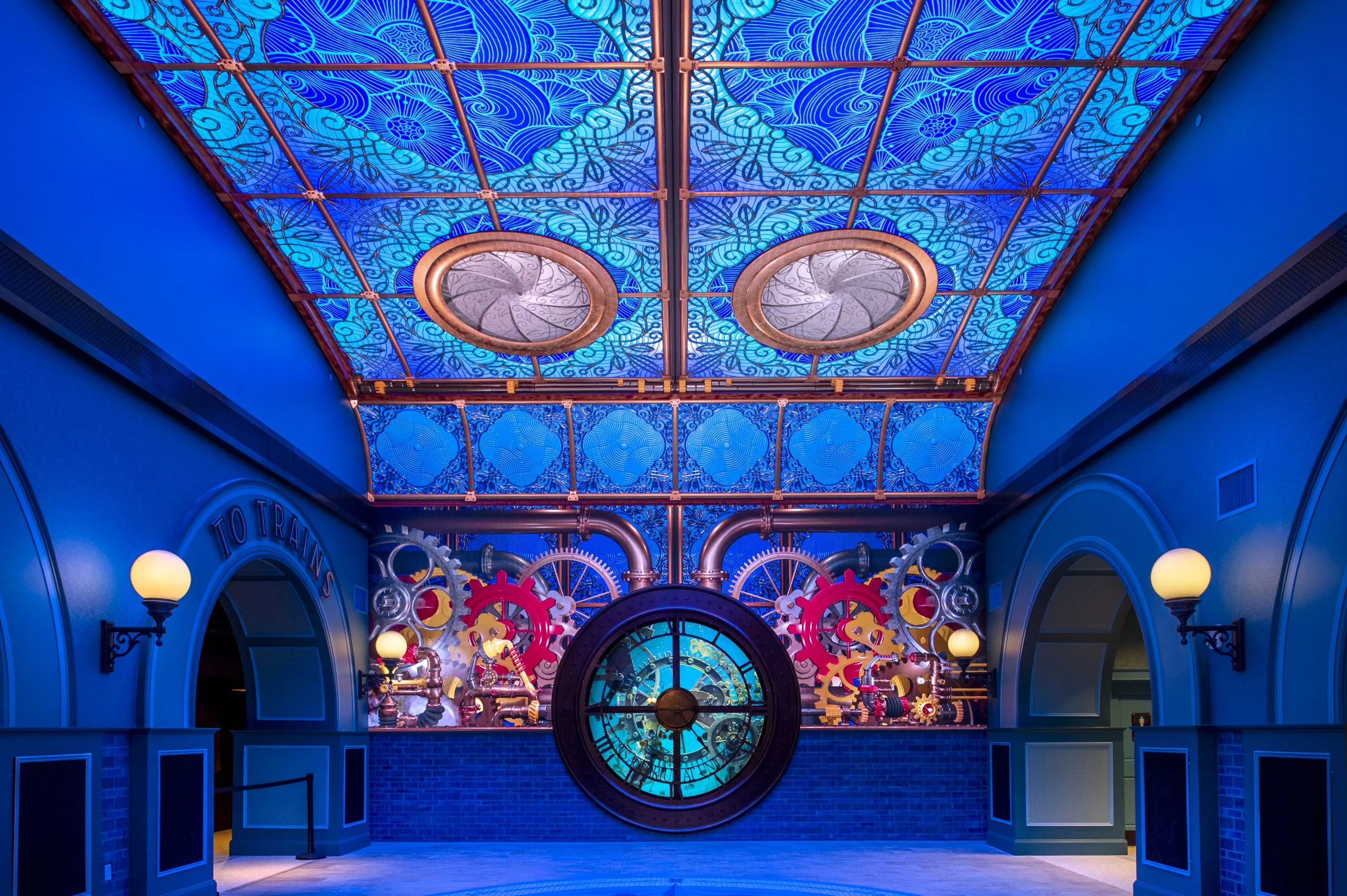 Blue-lit St. Louis Aquarium lobby with an ornate tiled ceiling, clock habitat and arched To Trains passages