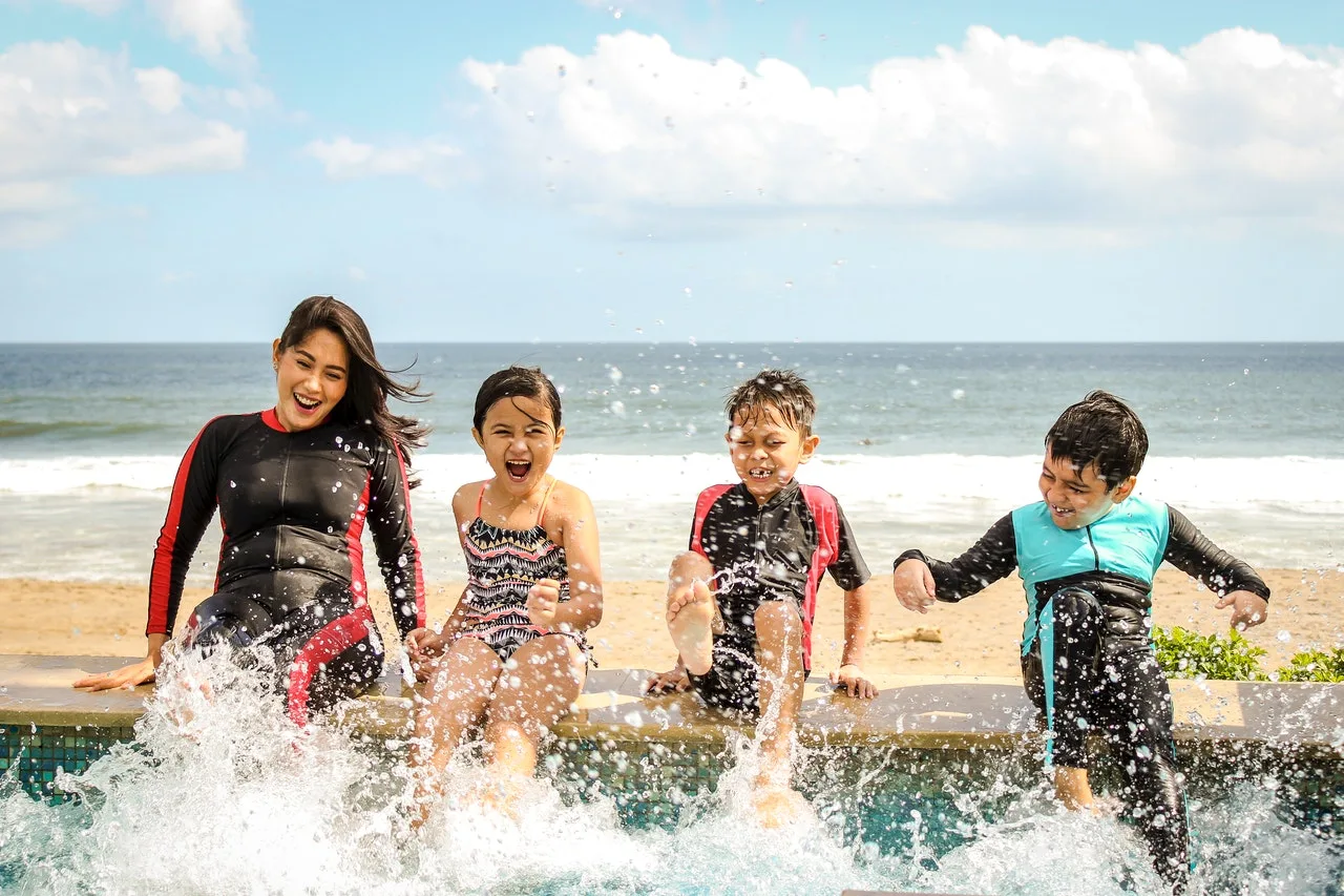 Mother and three children laughing as they kick water at the edge of a beachside pool