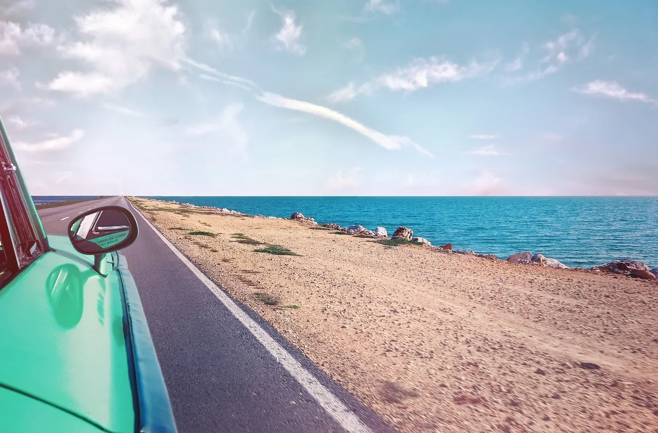 Vintage turquoise car on a coastal road beside a sandy beach and blue sea