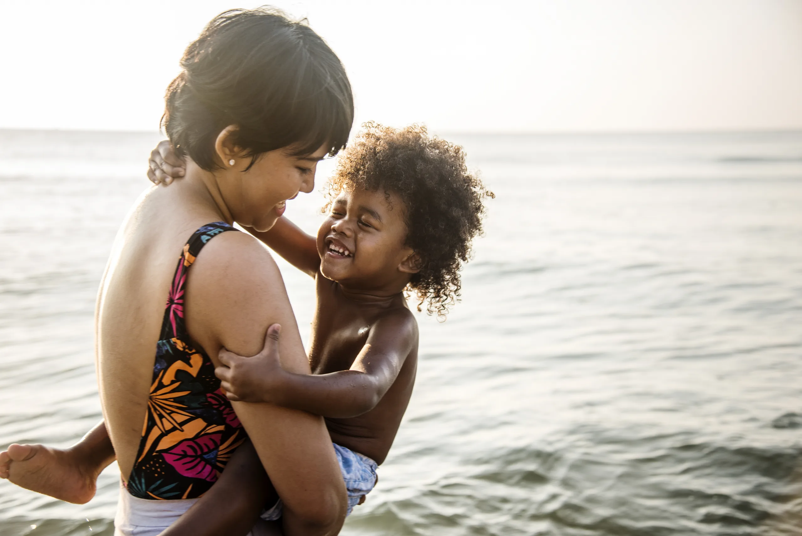 Mother laughing as she lifts her young child in the ocean shallows at the beach