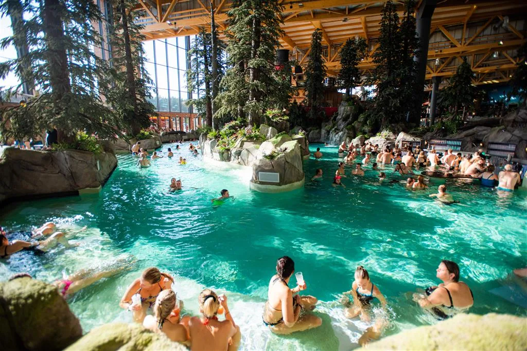 Bathers relaxing among waterfalls, rocks and evergreen trees in the Skog Lagoon at Rulantica, Europa-Park