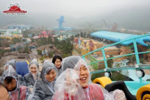 Guests ride a roller coaster at Chimelong Ocean Kingdom with a view of the main manta entry and whale shark icon in the background