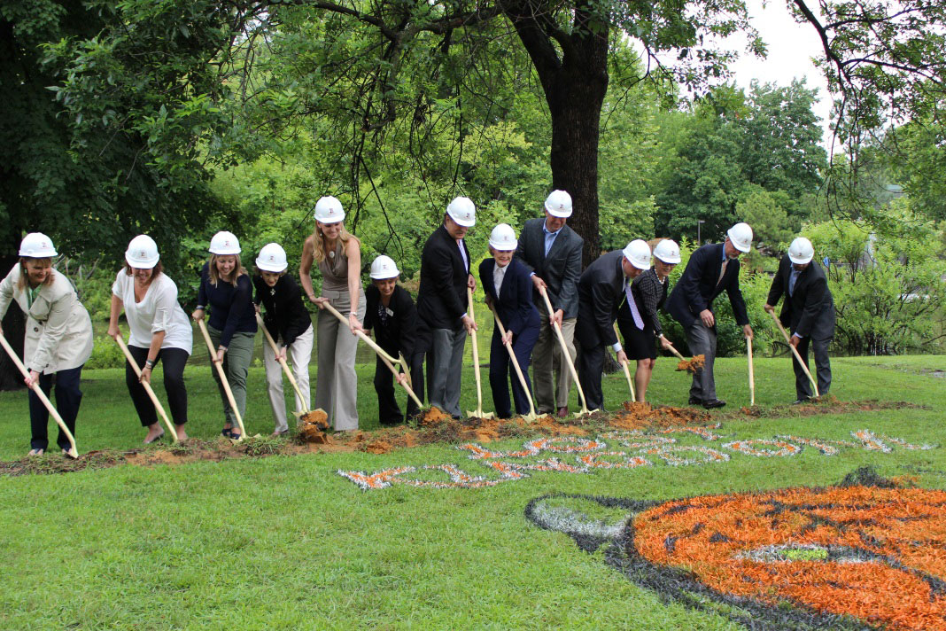 A line of people wearing hard hats break ground at Tulsa Zoo's Lost Kingdom