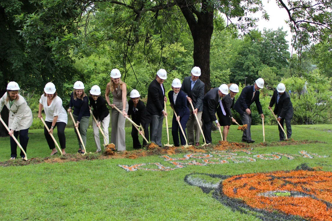 A line of people wearing hard hats break ground at Tulsa Zoo's Lost Kingdom