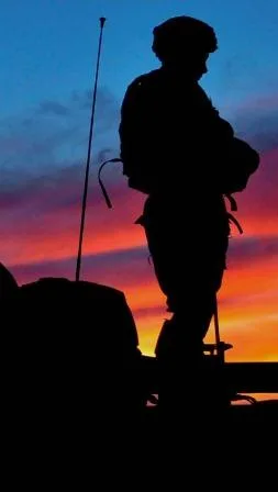 A soldier stands on a tank at sunset