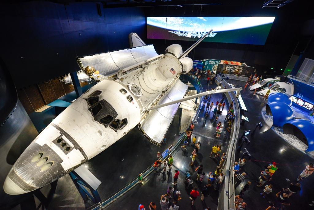View of Space Shuttle Atlantis on display at the Kennedy Space Center Visitor Complex with its cargo bay doors open and Canadarm extended, including other nearby exhibits and orbit camera