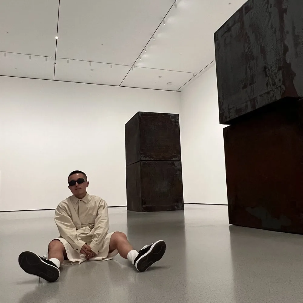 PGAV intern seated on the floor of a modern art gallery among large rusted steel sculptures