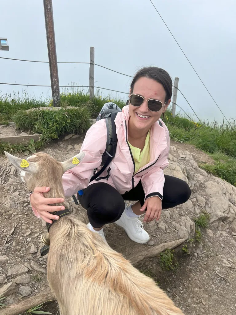 Carly Delay, PGAV intern, smiling while petting a goat on a hilltop hike