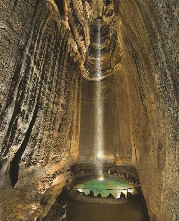 A massive underground waterfall pours into a lit pool in a cave at Ruby Falls