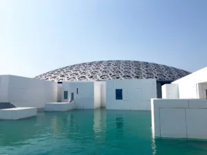 Lattice dome of the Louvre Abu Dhabi above its white gallery buildings and reflecting water