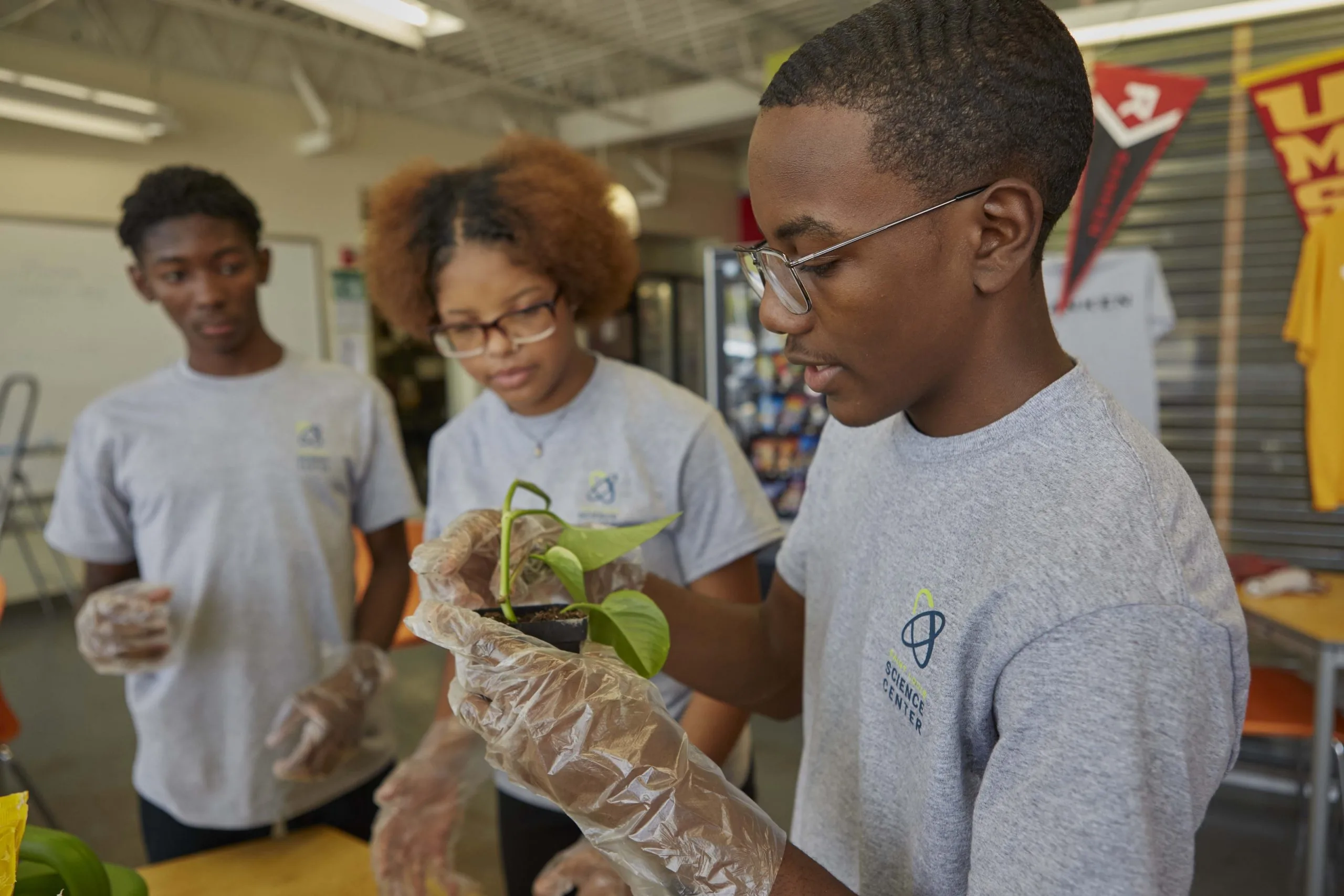 Youth Exploring Science students in gloves handling a potted plant at the Saint Louis Science Center
