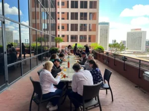 Team members sharing lunch at a long table on a sunny rooftop terrace overlooking downtown St. Louis
