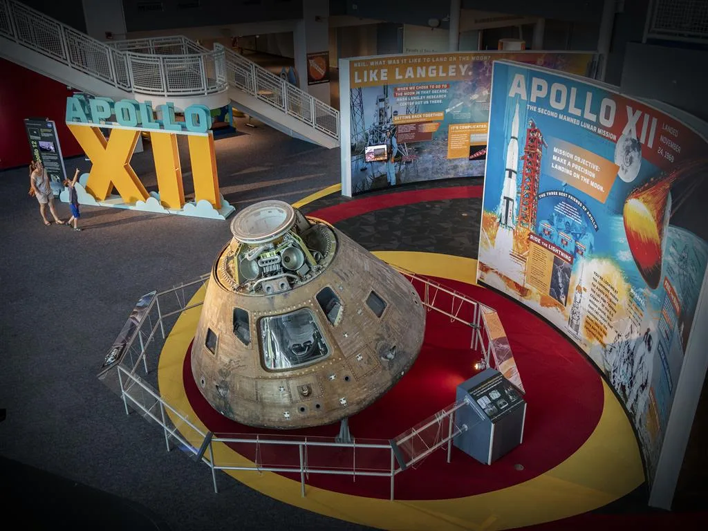 Apollo XII command module on a circular platform surrounded by curved graphic panels about the second Moon landing