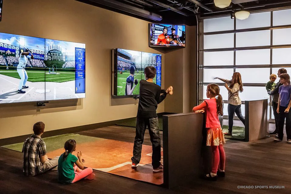 Kids taking turns at interactive batting and football simulators at the Chicago Sports Museum