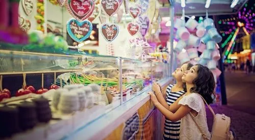 Two girls gazing at a candy stand full of sweets and gingerbread hearts at a fair