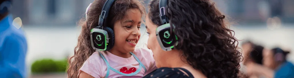 Girl and woman smiling in glowing silent disco headphones at a quiet event