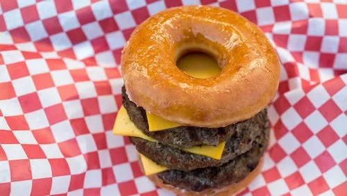 Double cheeseburger served on a glazed doughnut bun on a red checkered paper, a classic fair food