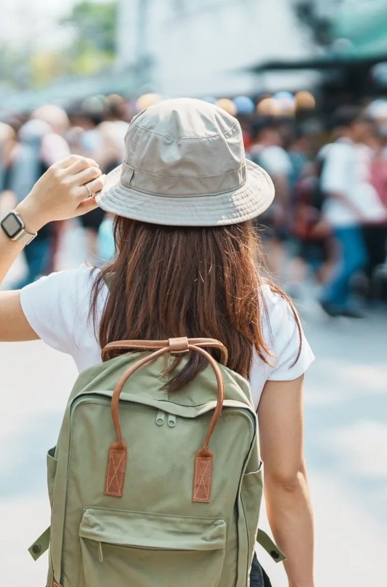 Traveler in a bucket hat and backpack checking her watch on a crowded street