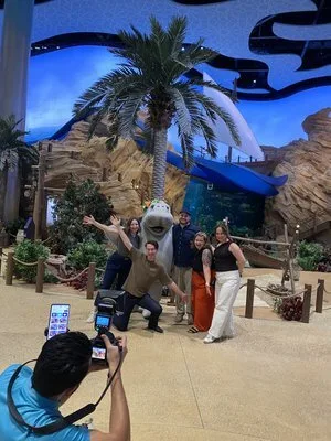 PGAV team members posing with a shark character in a palm-lined plaza at SeaWorld Abu Dhabi