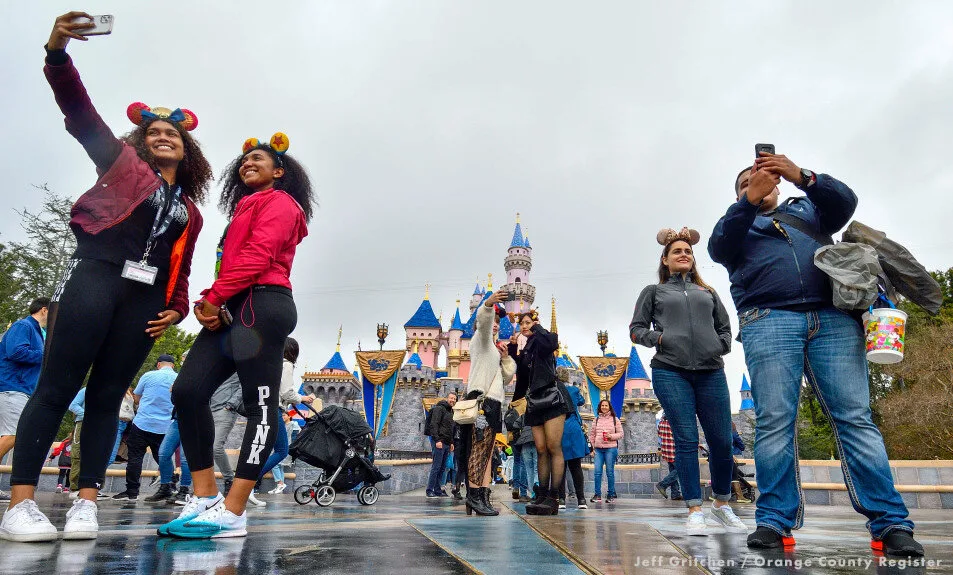 Visitors in Mickey ears taking selfies in front of Sleeping Beauty Castle at Disneyland