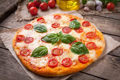 Margherita pizza topped with fresh tomatoes, mozzarella and basil on a rustic wooden table