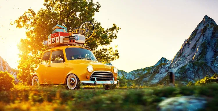 Yellow retro car loaded with luggage and a bike on a country road at sunset
