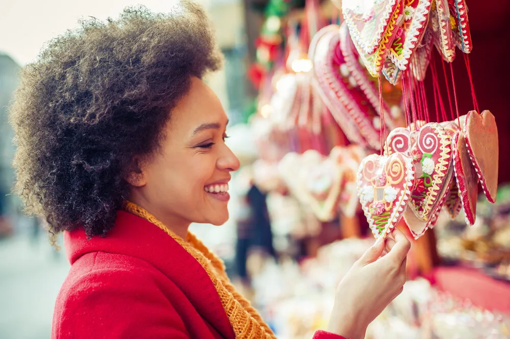 Smiling woman browsing decorated gingerbread hearts at a market stall